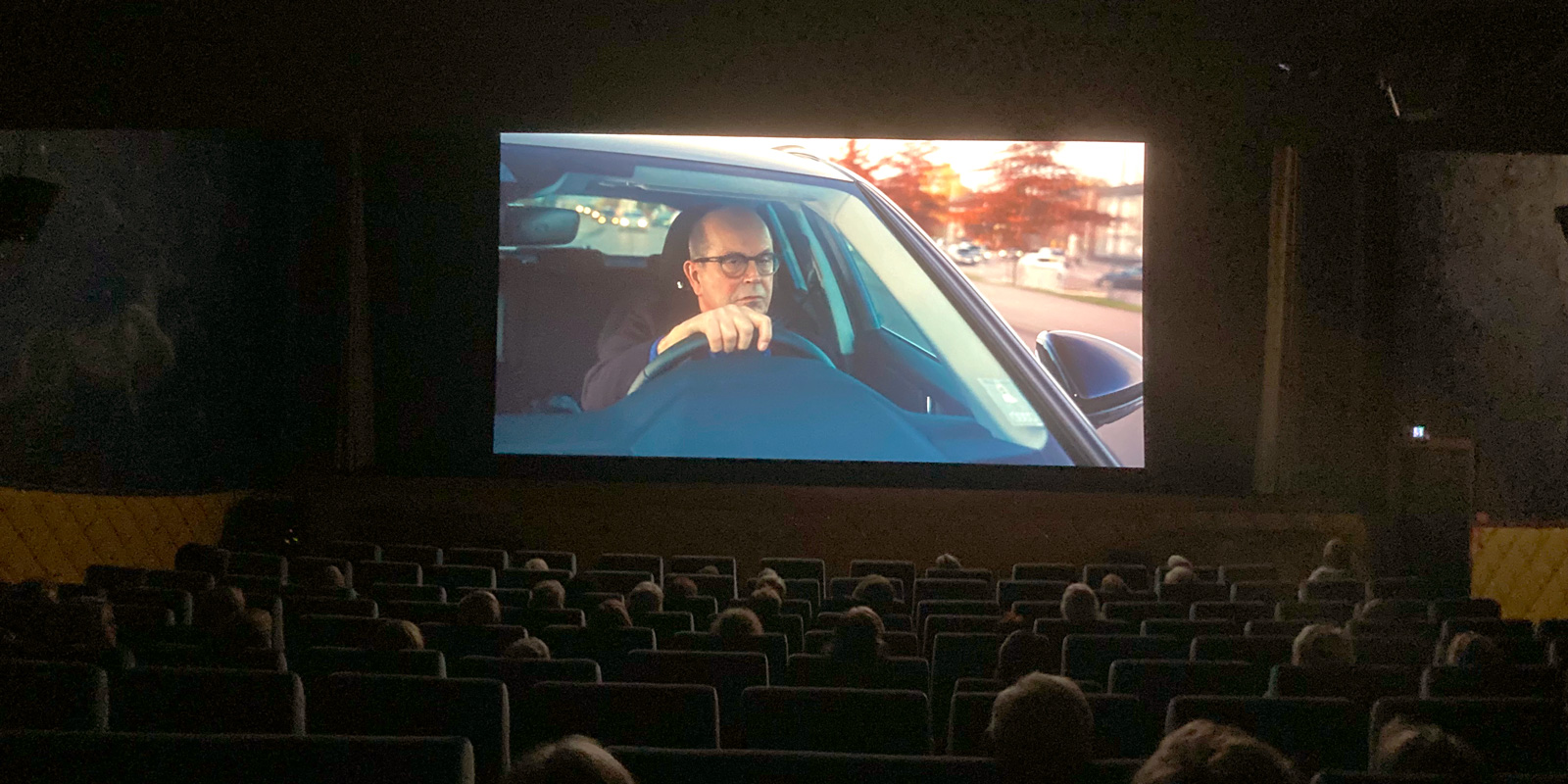 Folk i biosalongen och en scen ur filmen visas på bioduken.